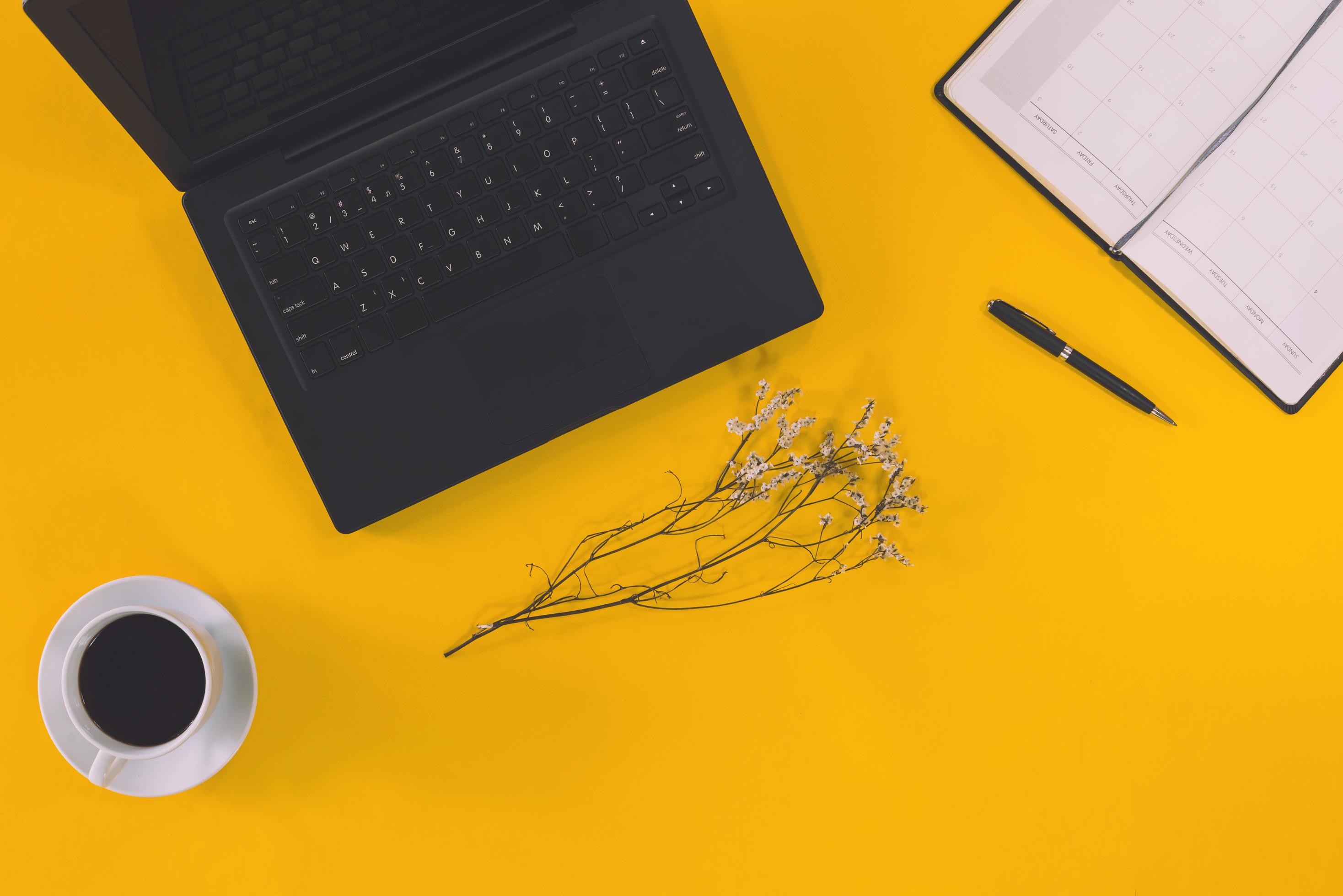 Conceptual workspace Laptop computer and coffee cup note book with White flowers placed on the table on pastel background yellow. Stock Free