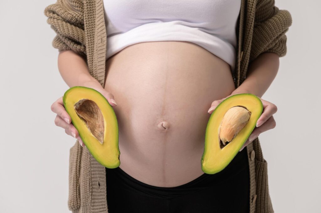 Portrait of Beautiful pregnant woman holding avocado over white background studio, health and maternity concept Stock Free