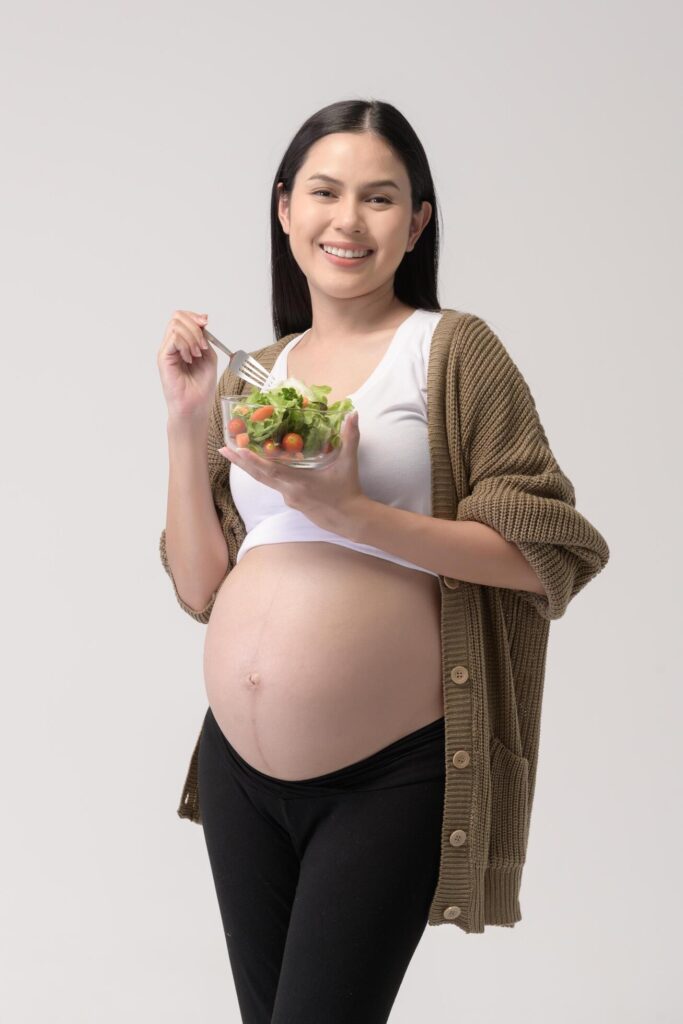 Portrait of Beautiful pregnant woman eating salad over white background studio, health and maternity concept Stock Free