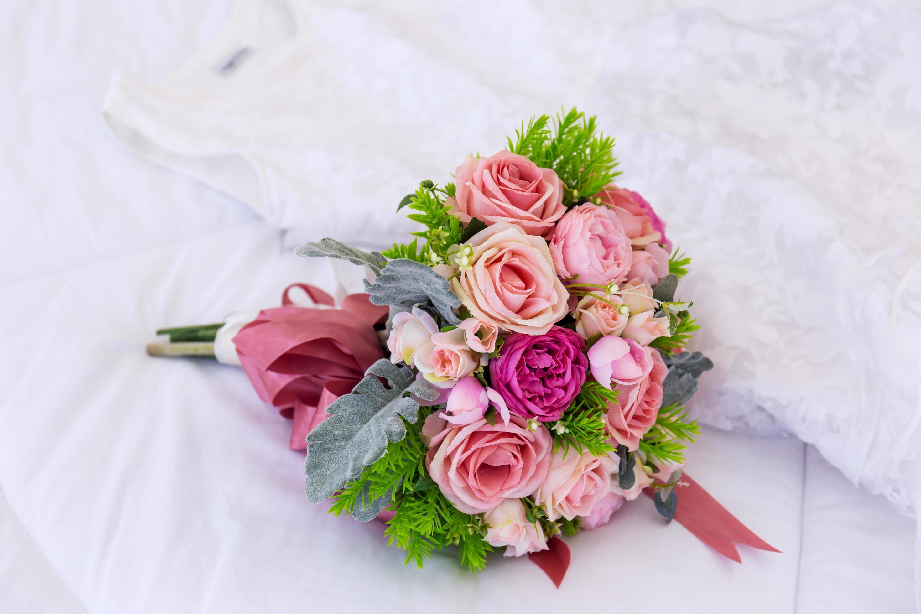 A beautiful bouquet of flowers was laid out on a clean, white bed. Next to the bridal gown were placed together. Stock Free