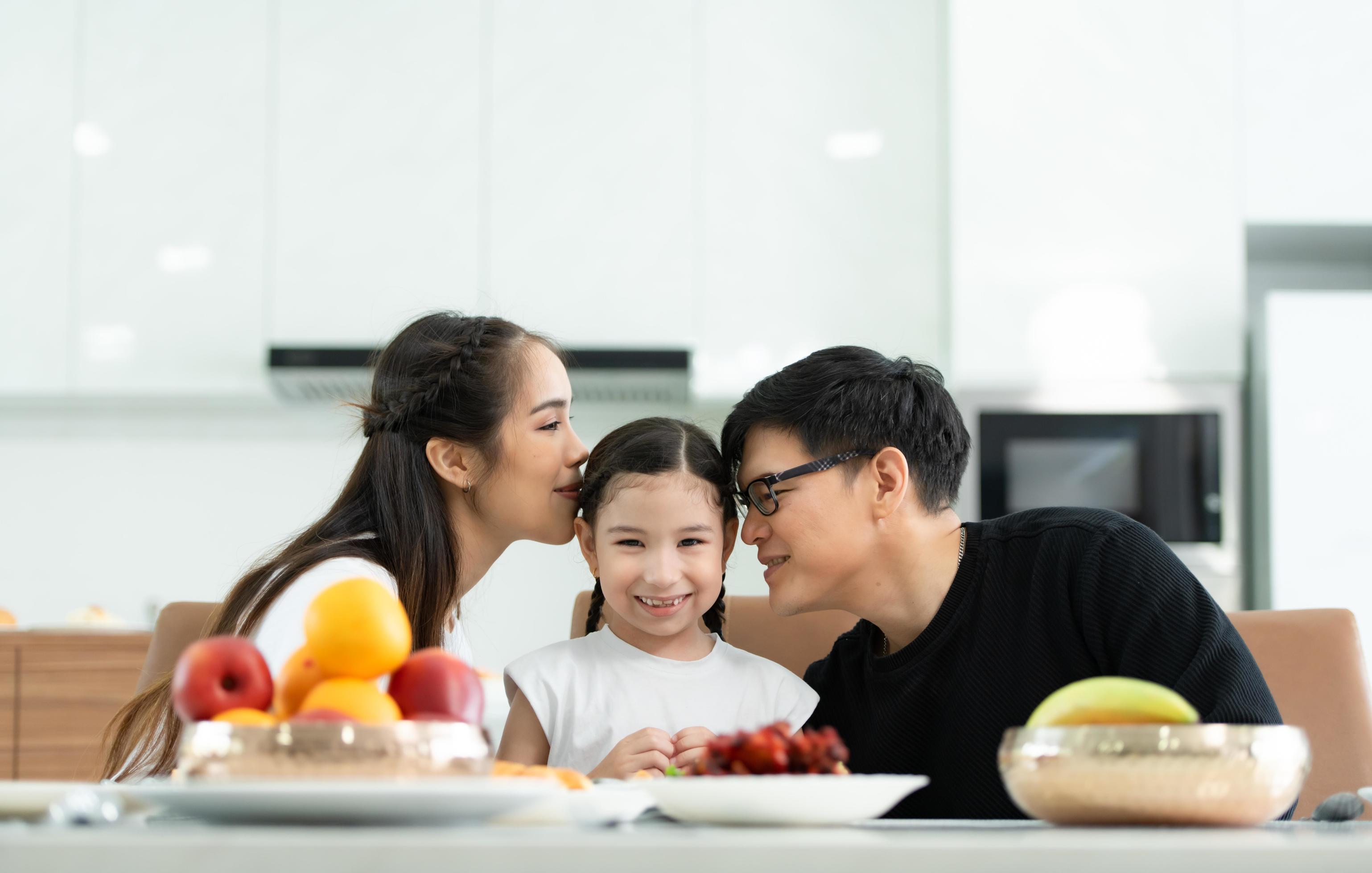 Asian father and mother Show your love to little daughter and having breakfast together happily in the dining room of the house. Stock Free