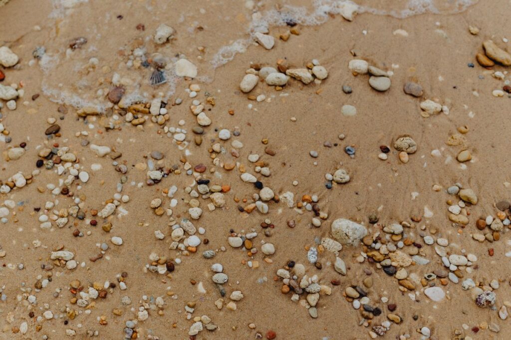 Sand beach background with sea shells & pebbles – many round small stones Stock Free