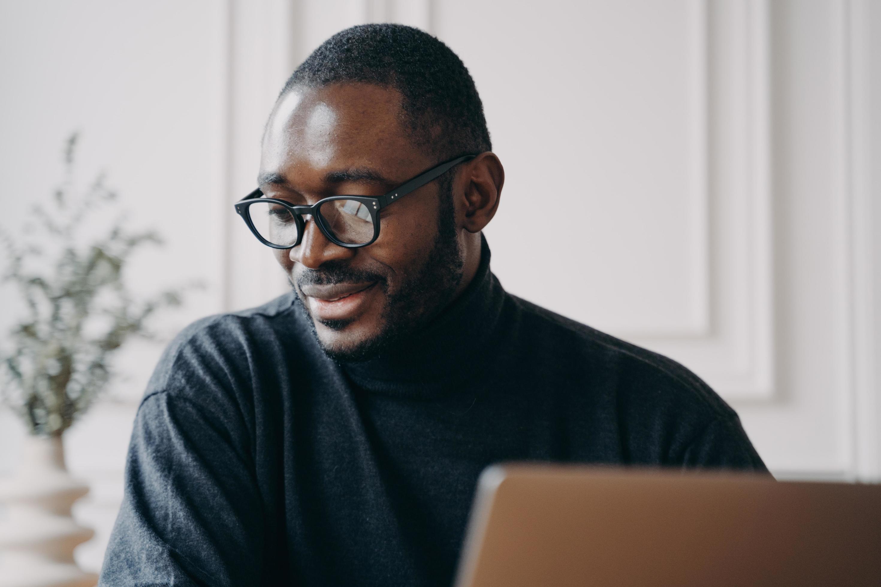 Pensive Afro american man sits at desk at home, watches online video class or webinar on computer Stock Free