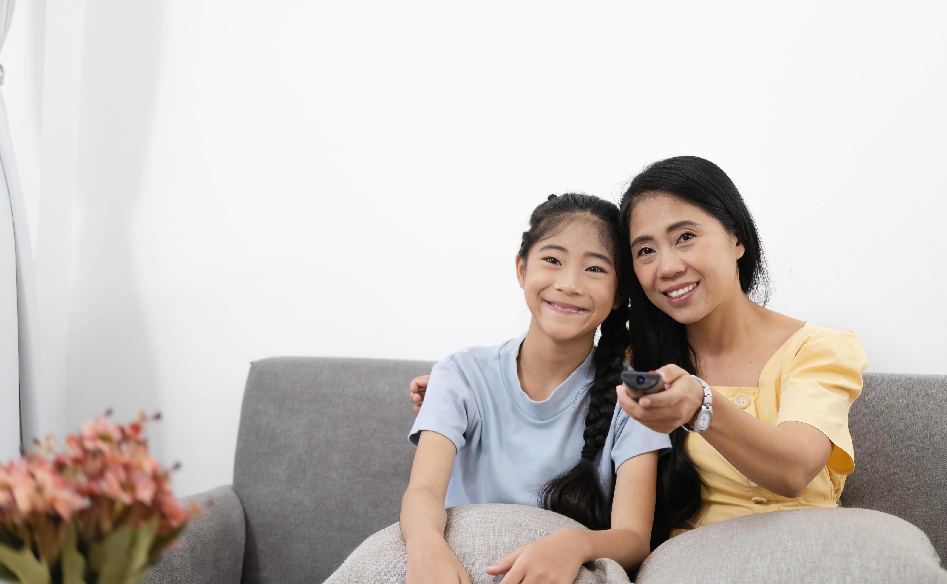 Happy asian parents sit on comfortable couch in living room with little kids watch TV enjoy home weekend enjoying movie Stock Free