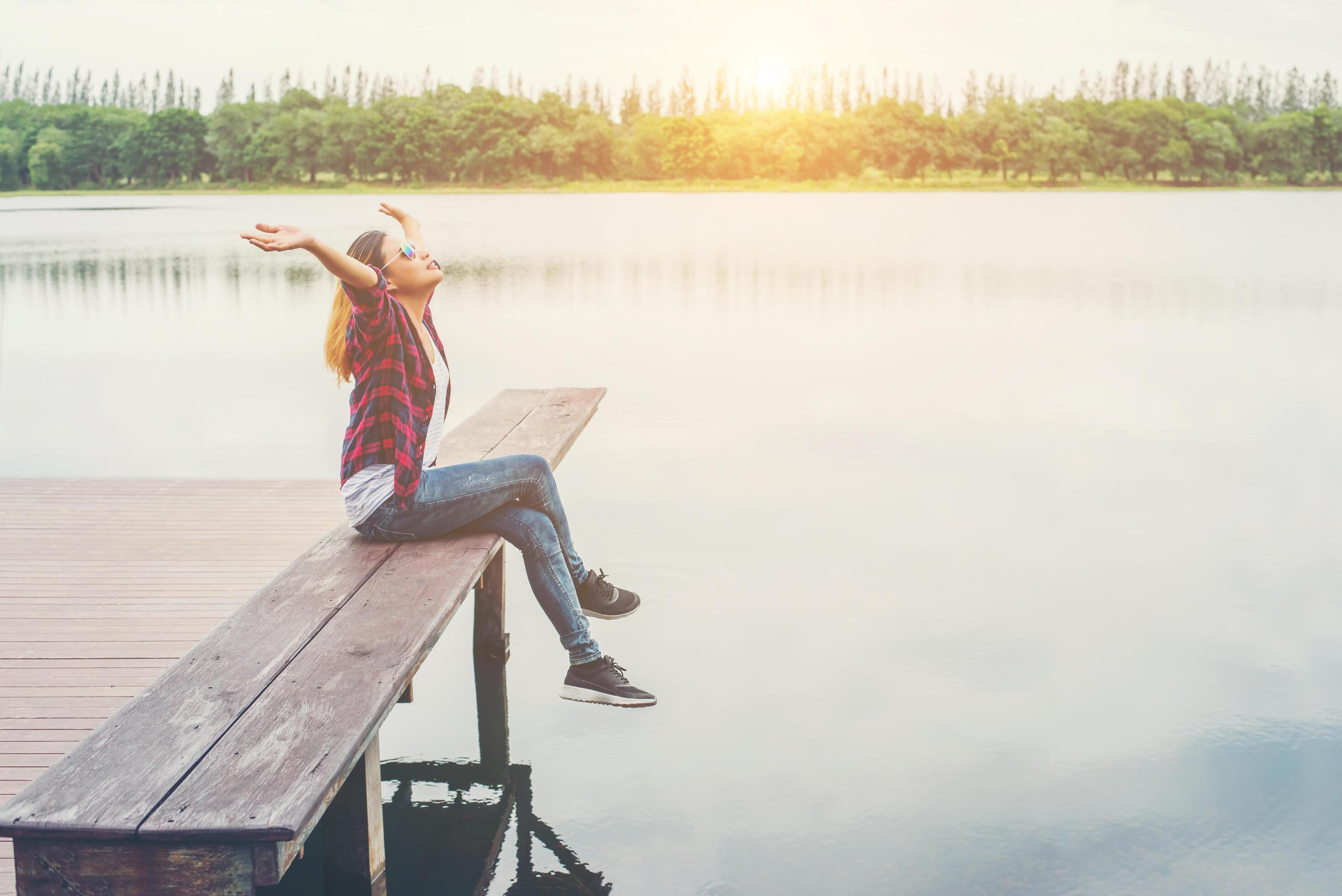 Young hipster woman sitting on pier raised hands,relaxing with natural freedom,enjoy and happy. Stock Free