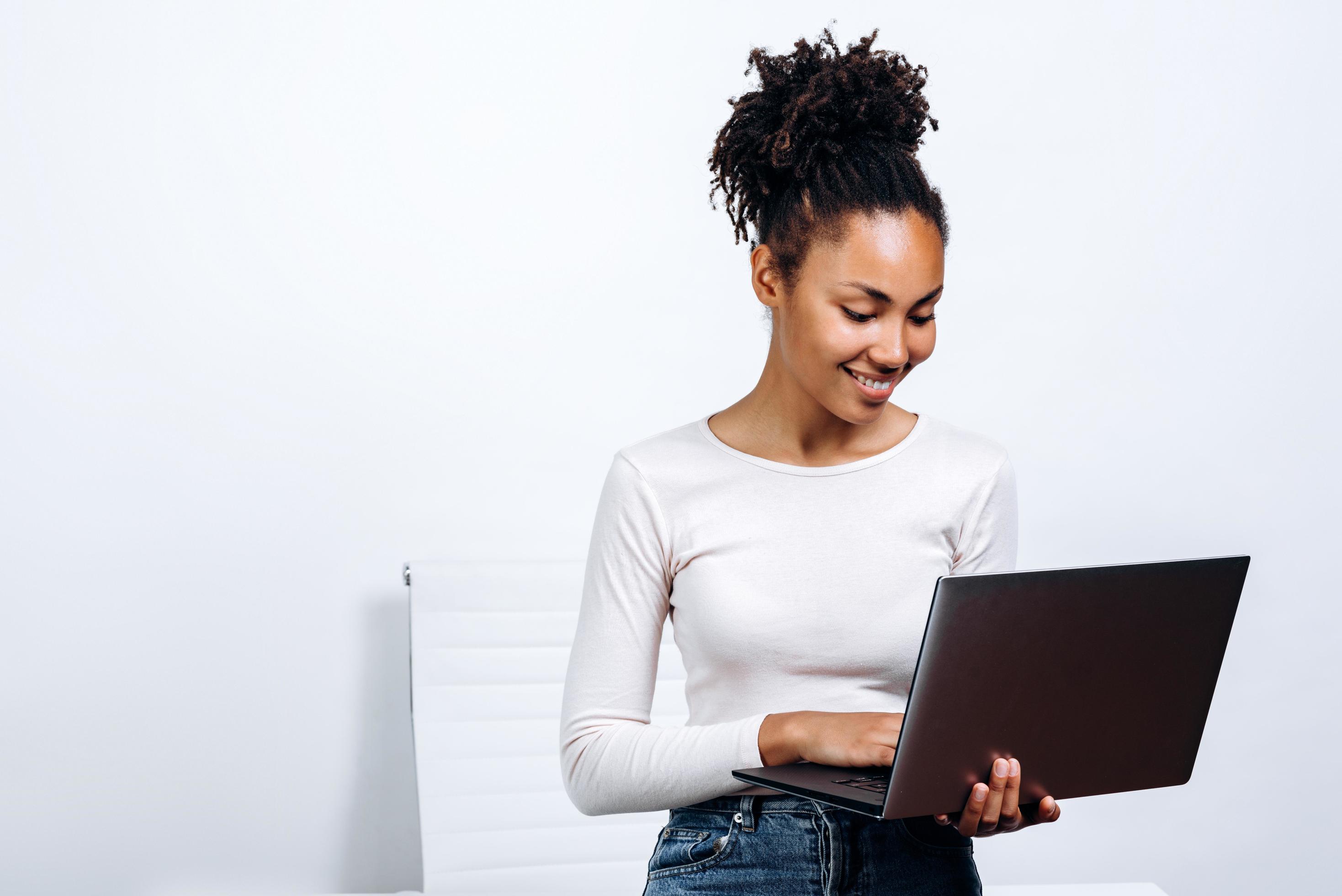 Photo of young cheerful business woman standing over white wall with laptop computer. Stock Free