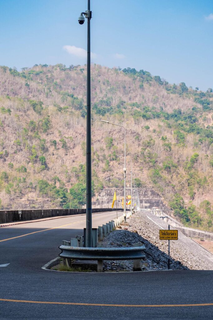 The scene of the road at the top of the dam, with the mountains in the background and a light pole. Stock Free