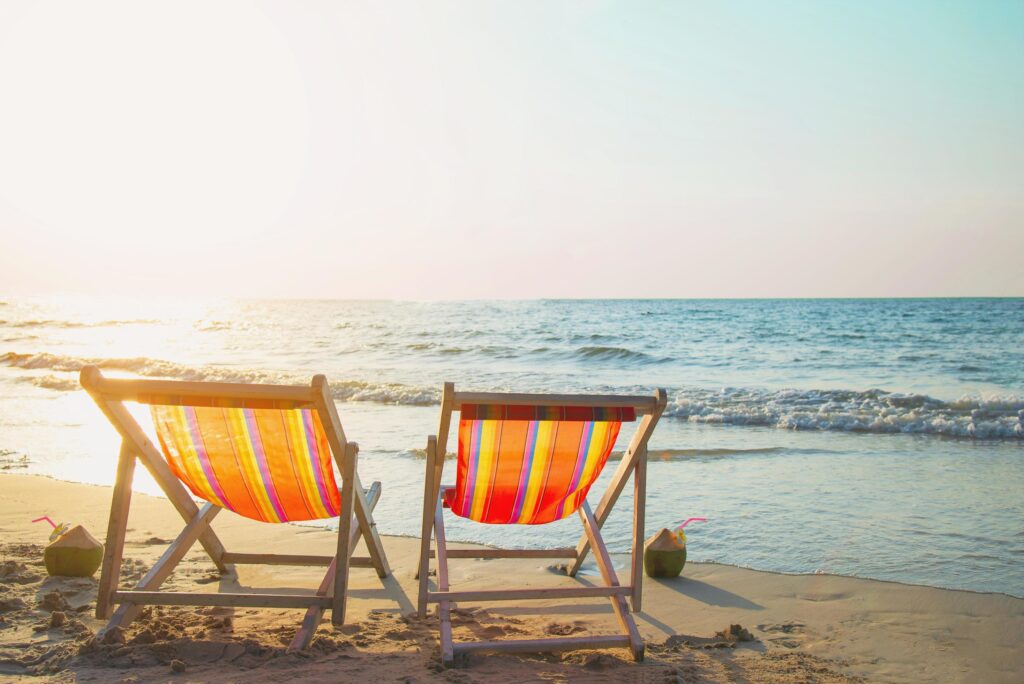 Couple relax chair on sand beach with warm sunset – vacation in beautiful sea nature concept Stock Free