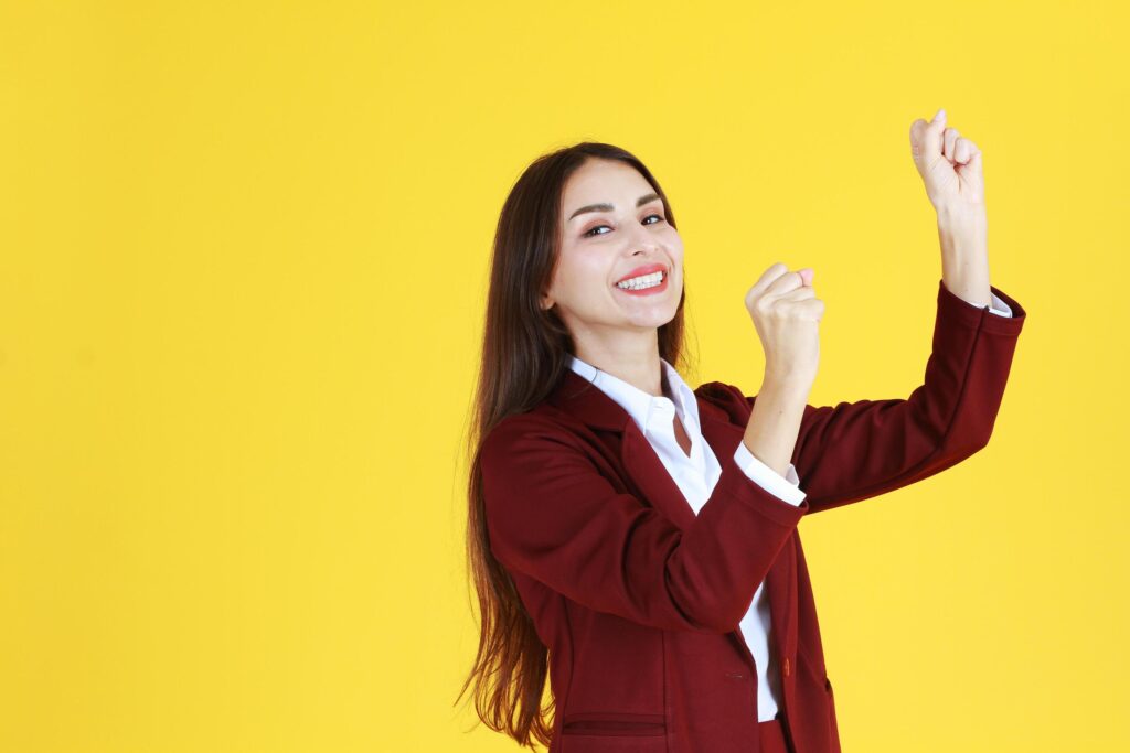 Successful Businesswoman smile and raised her hand for success in jobs isolated on yellow background Stock Free