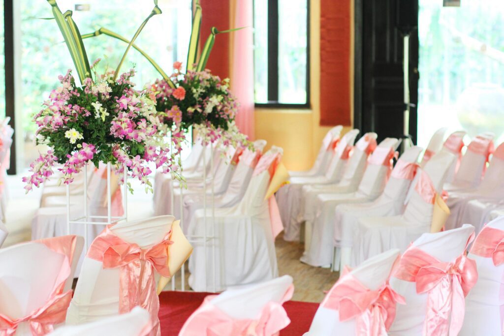 Beautiful chairs decoration with pink ribbon and Bouquet of orchids with flowers in a vase in wedding event hall. Stock Free