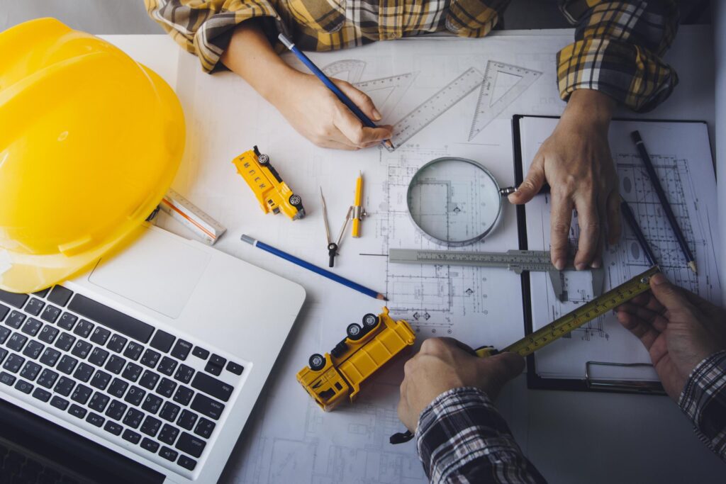 Two colleagues discussing data working and tablet, laptop with on on architectural project at construction site at desk in office Stock Free