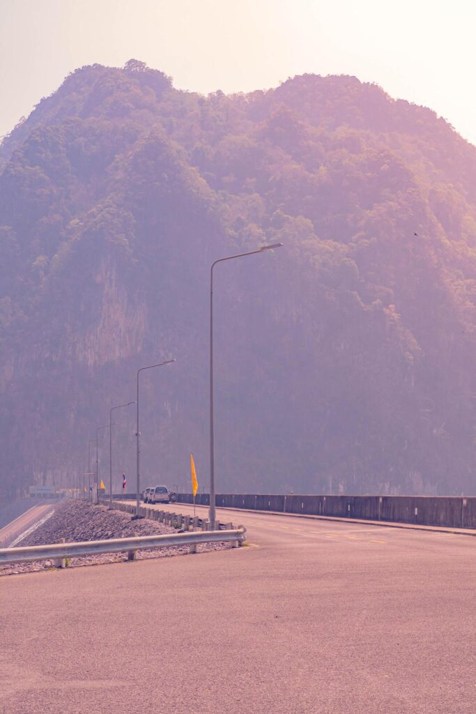 The scene of the road at the top of the dam, with the mountains in the background and a light pole. Stock Free