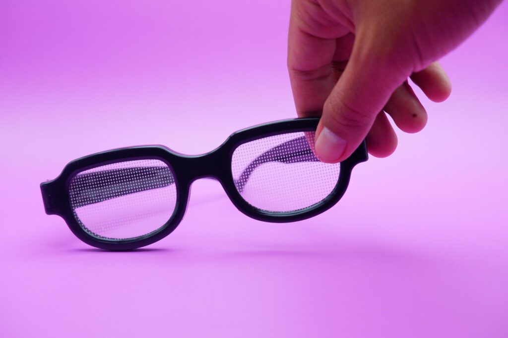 hand holding black frame glasses. black frame glasses isolated on purple background. black frame glasses with curved frames and transparent glass. Stock Free