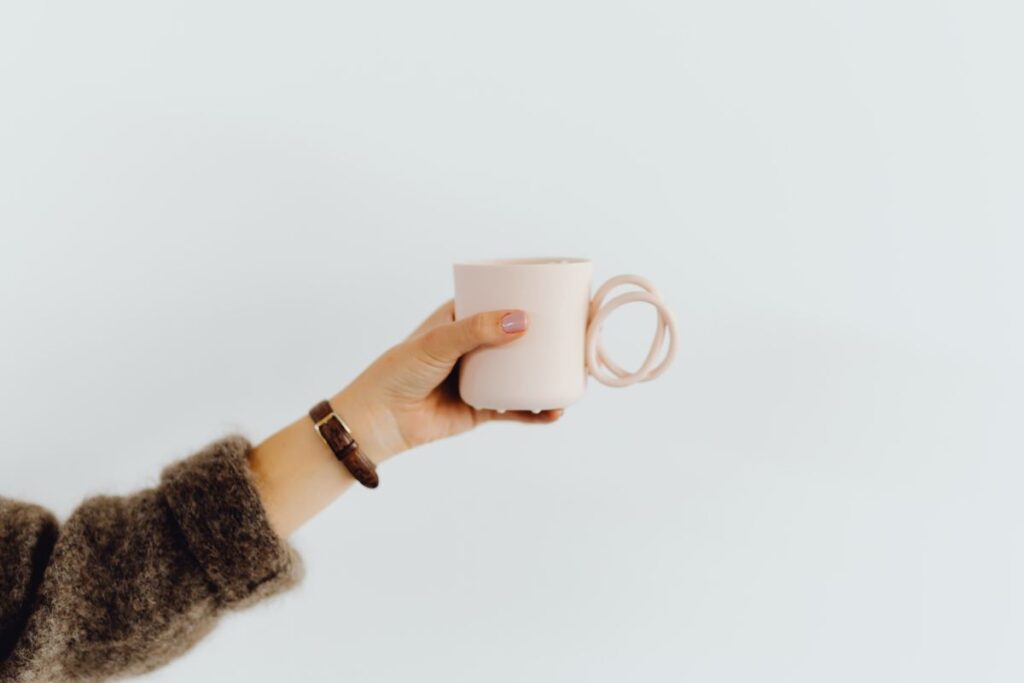 A woman in a brown sweater holds a pink, minimalist mug Stock Free