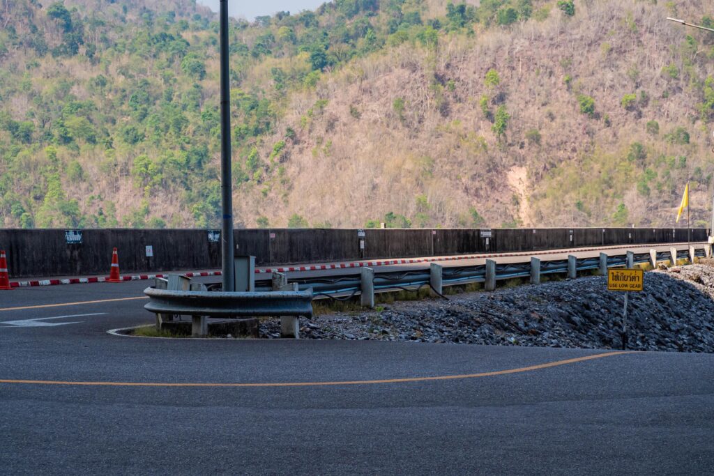 The scene of the road at the top of the dam, with the mountains in the background and a light pole. Stock Free