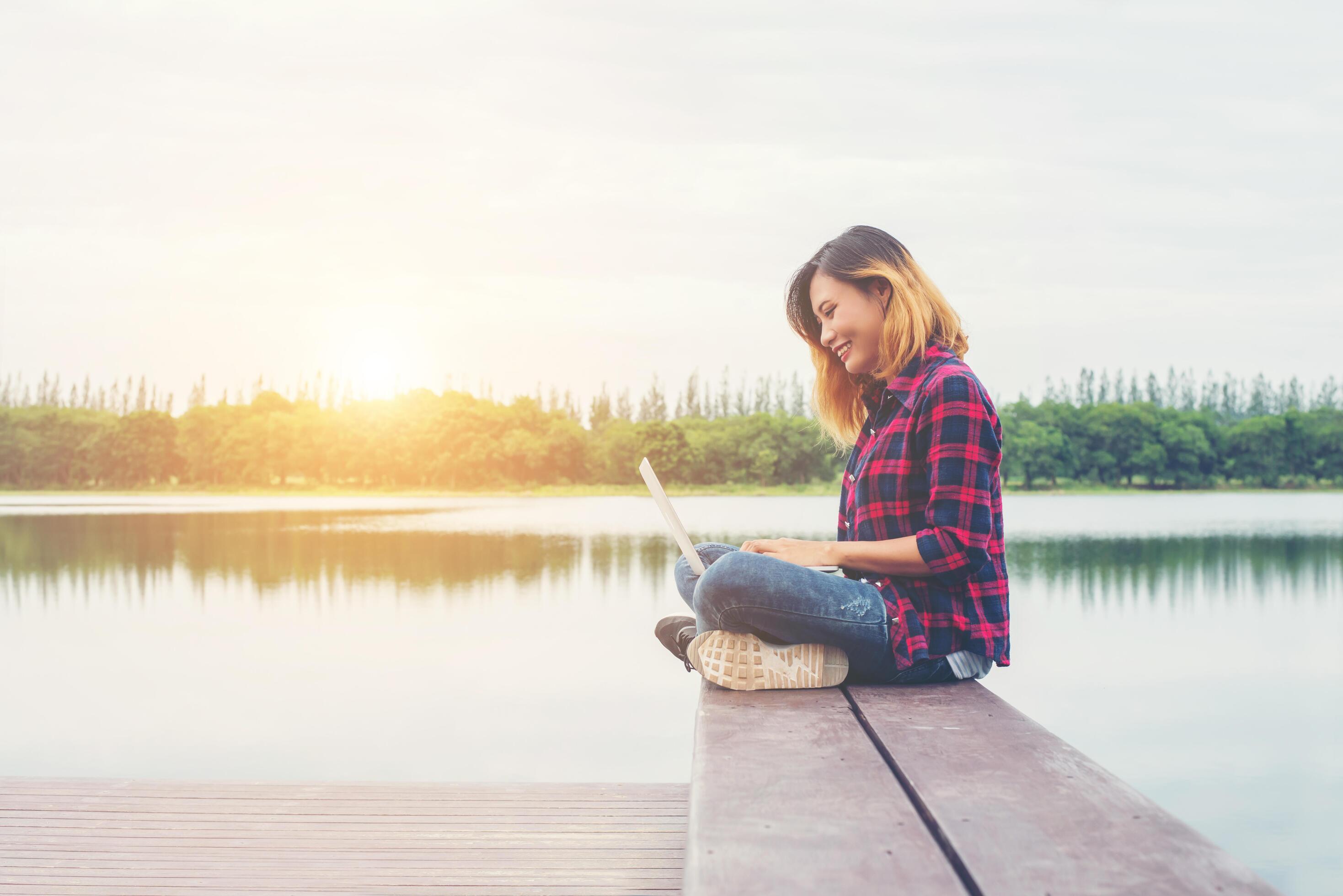 Young happy hipster woman working with her laptop sitting on pier,relaxing enjoy with nature. Stock Free