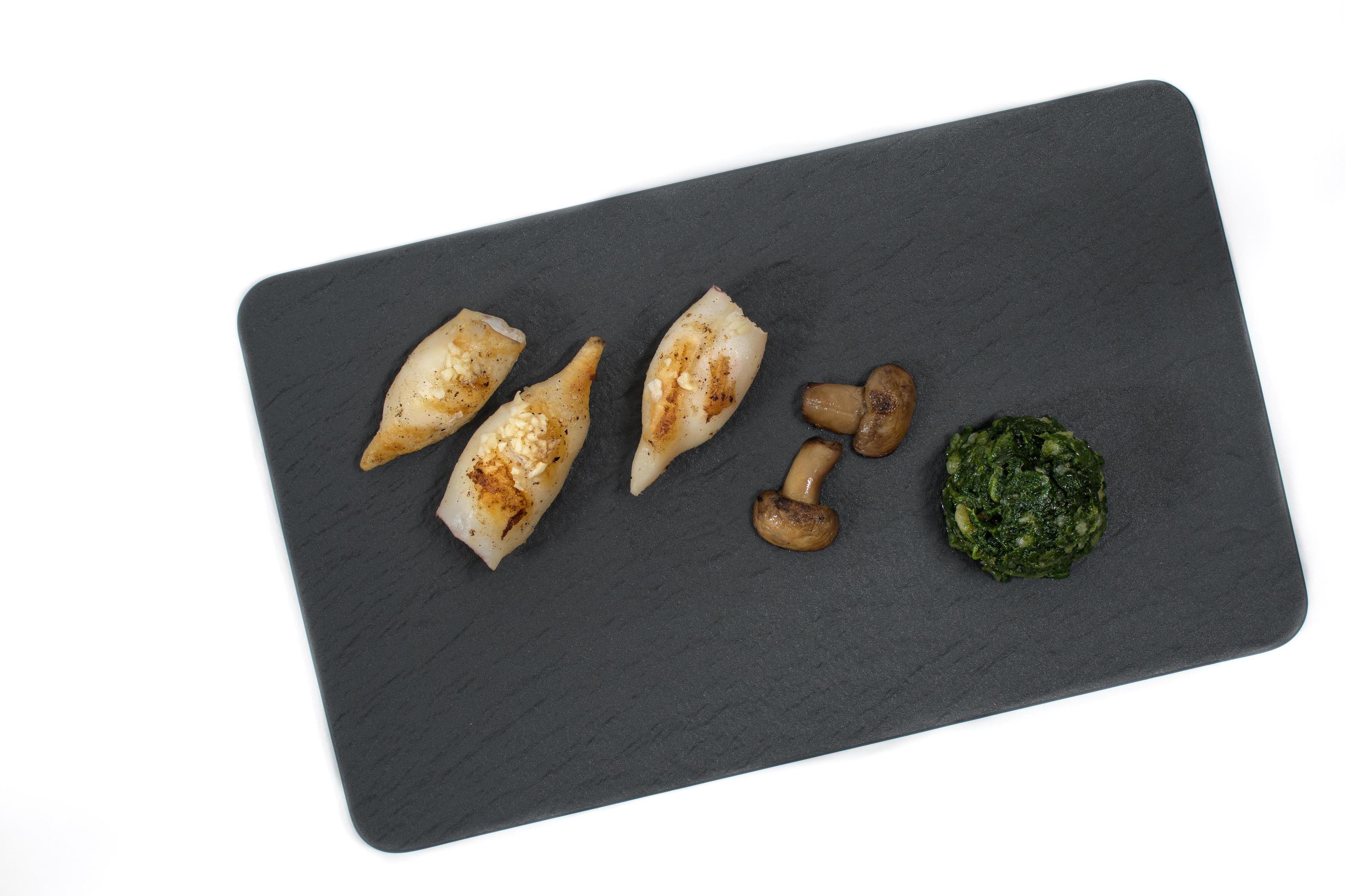 Flat lay image of sea food grilled squid with mushrooms and Swiss chards on a black stone plate Stock Free