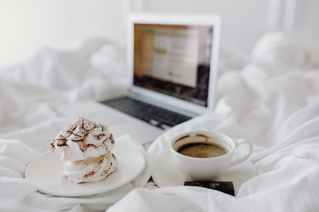 Woman working on a laptop while enjoying a breakfast coffee and chocolate in bed Stock Free