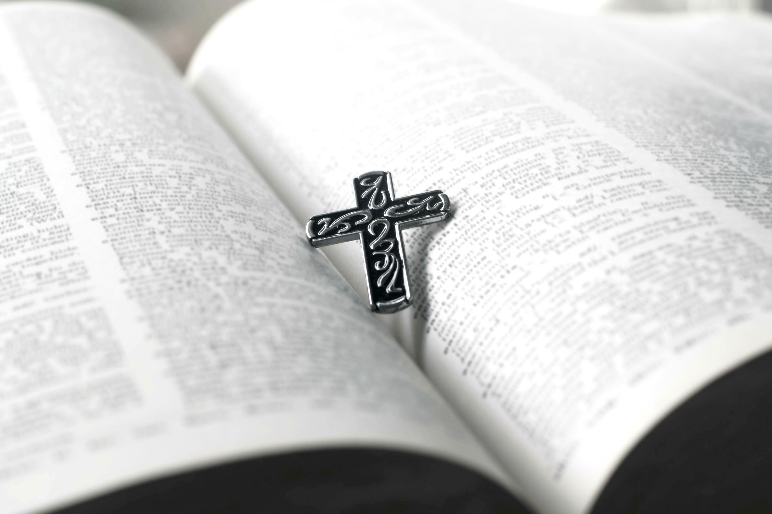 Closeup image of metal cross which places on opending bible book, soft focus, concept for religious lifestyle of christian people around the world. Stock Free