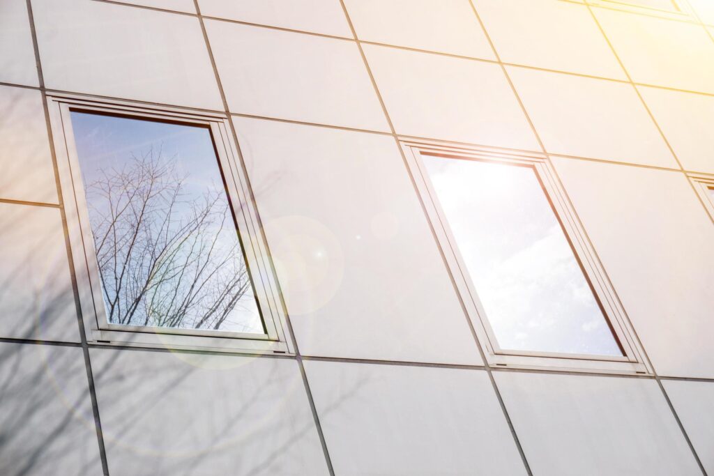 Closeup and crop reflection and shadow of winter tree and bright blue sky on office building windows with sun and lens flare. Stock Free