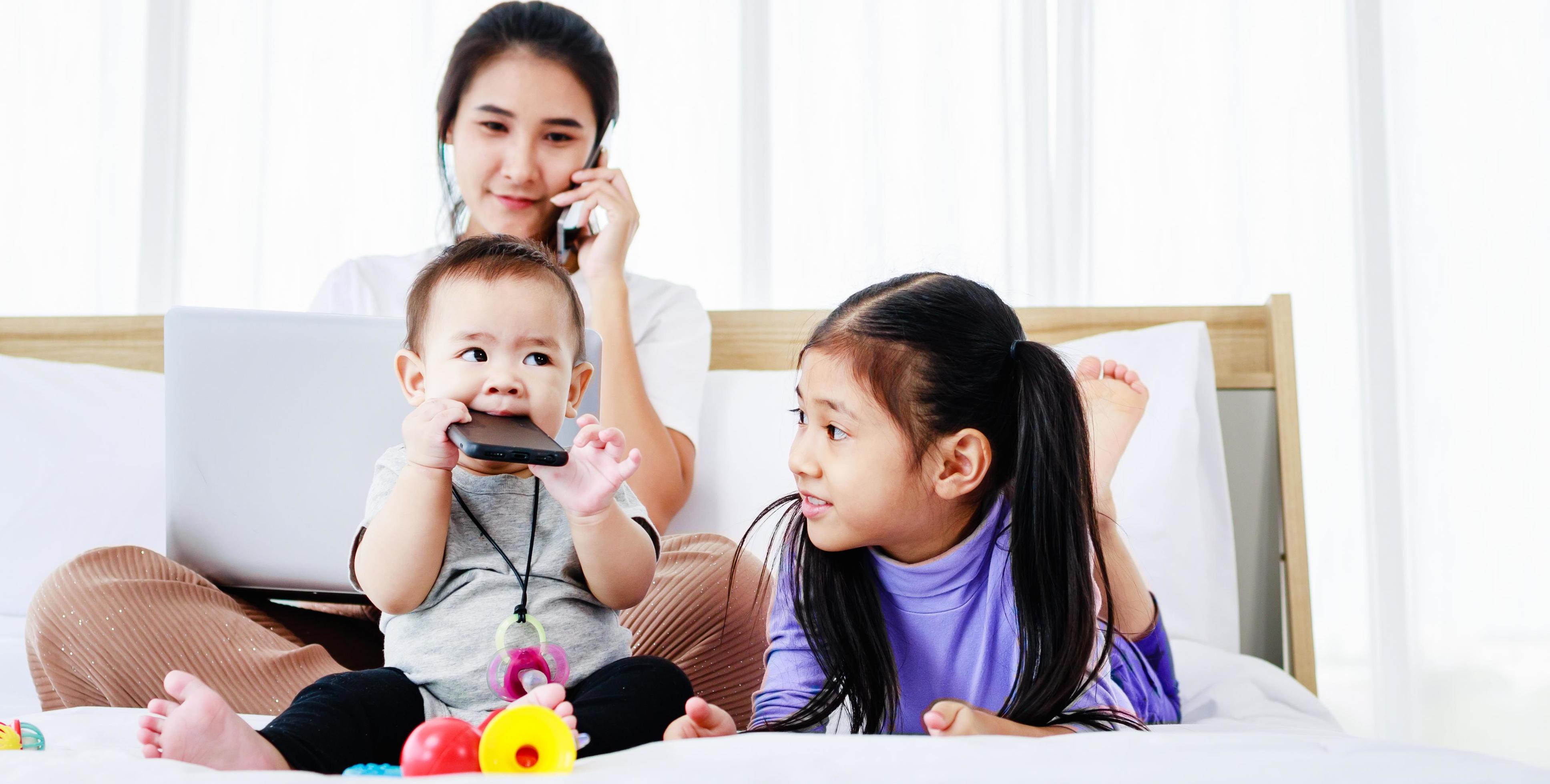 Busy freelancer mother working on laptop and caring for her baby and little daughter Stock Free