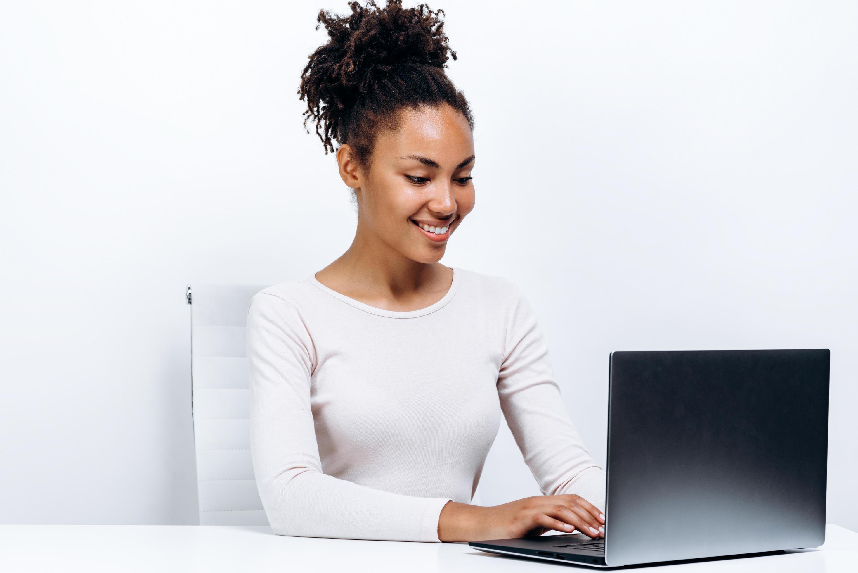 Happy young woman sitting at the table and using laptop on a white background Stock Free