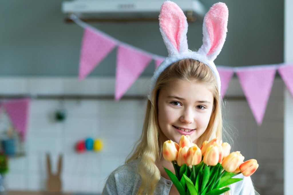 Little girl in holding tulips in white bunnys earrs in hands. Adorable smiling little girl holding flowers. Stock Free