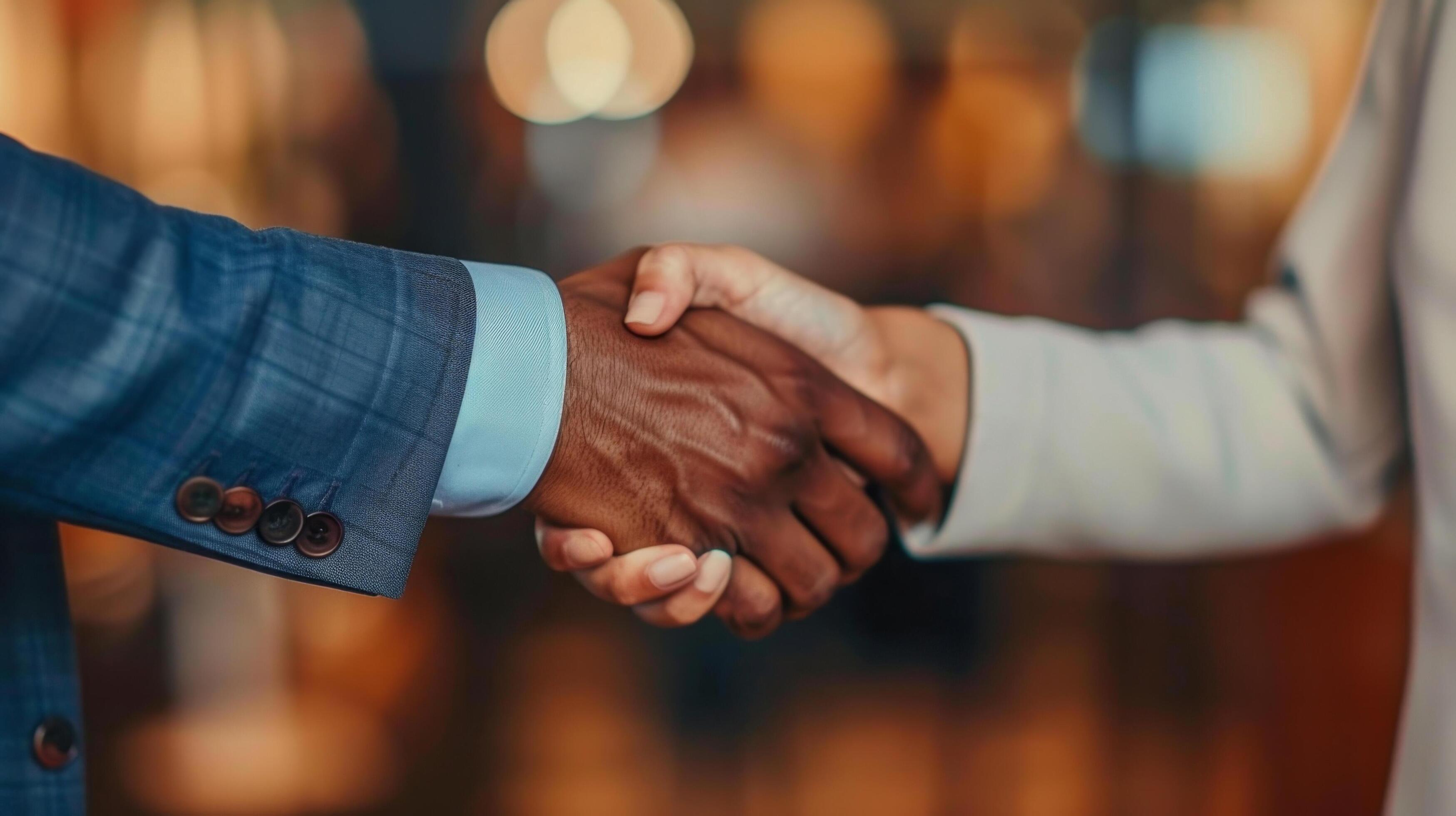 Close-up of two individuals from diverse backgrounds shaking hands, symbolizing partnership and business agreement in a professional setting. Stock Free