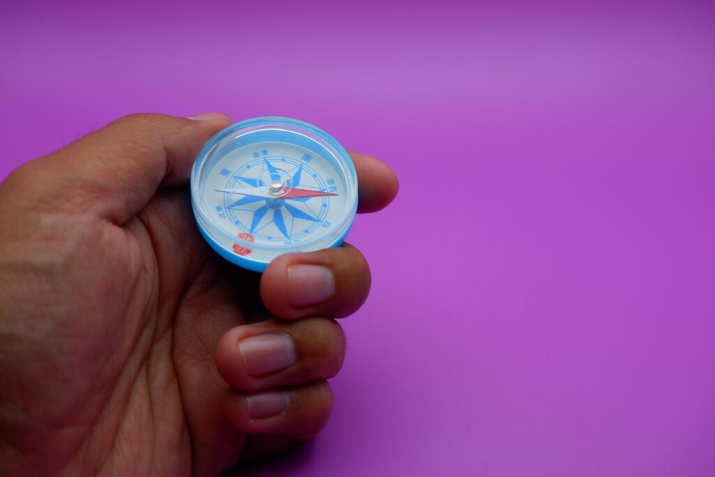 hand holding a compass isolated on a purple background Stock Free