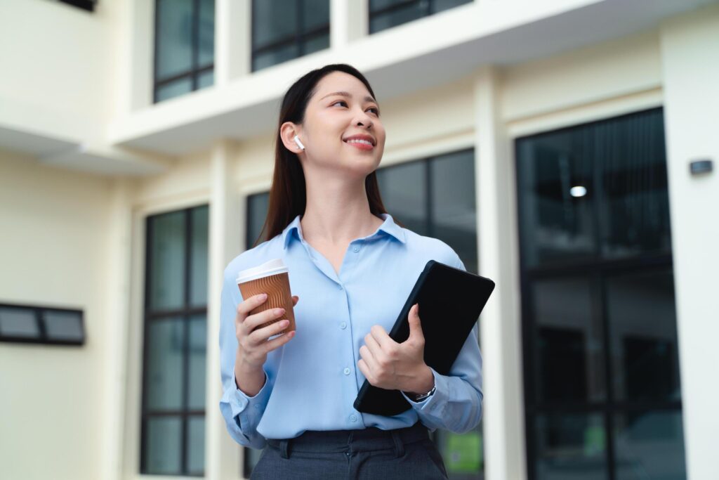 A business woman is standing in the city with a cup of coffee and a tablet Stock Free