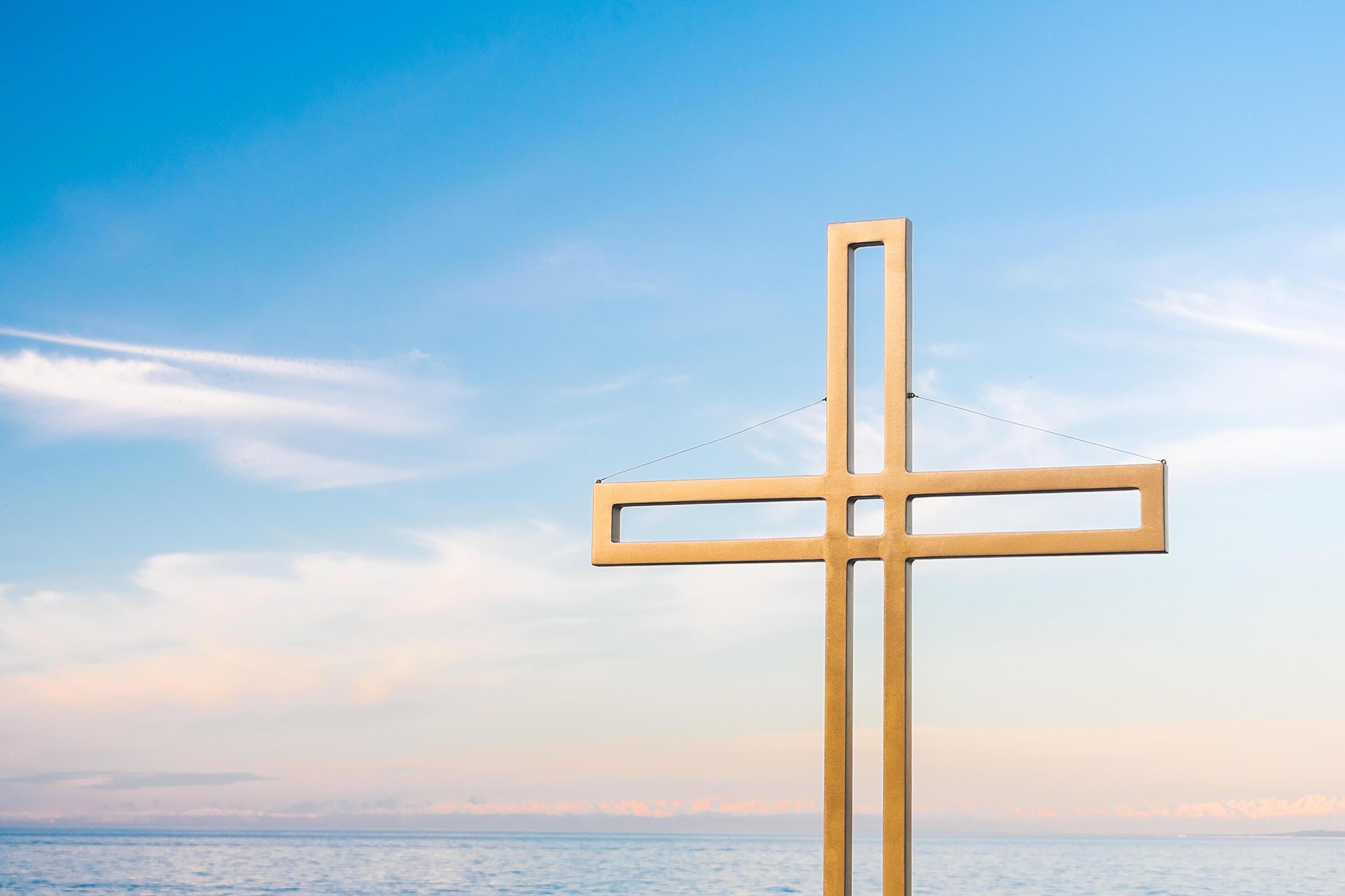 Golden cross against a background of blue sky with clouds. A minimalistic view of a gold-colored cross against the sky. Stock Free