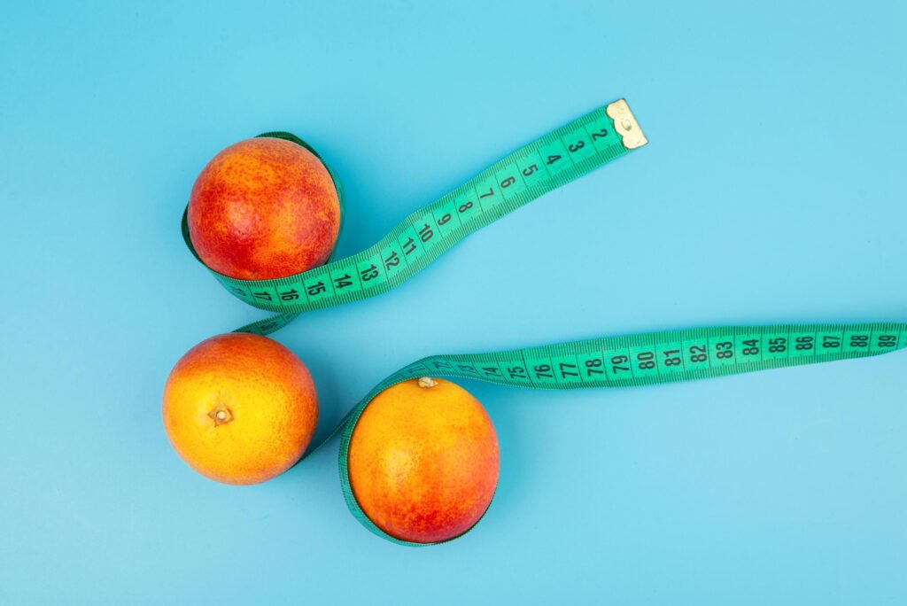 A red-orange tangerine wrapped in a measure tape on a light blue background. diet and healthy food concept. Bloody orange. Top view Stock Free