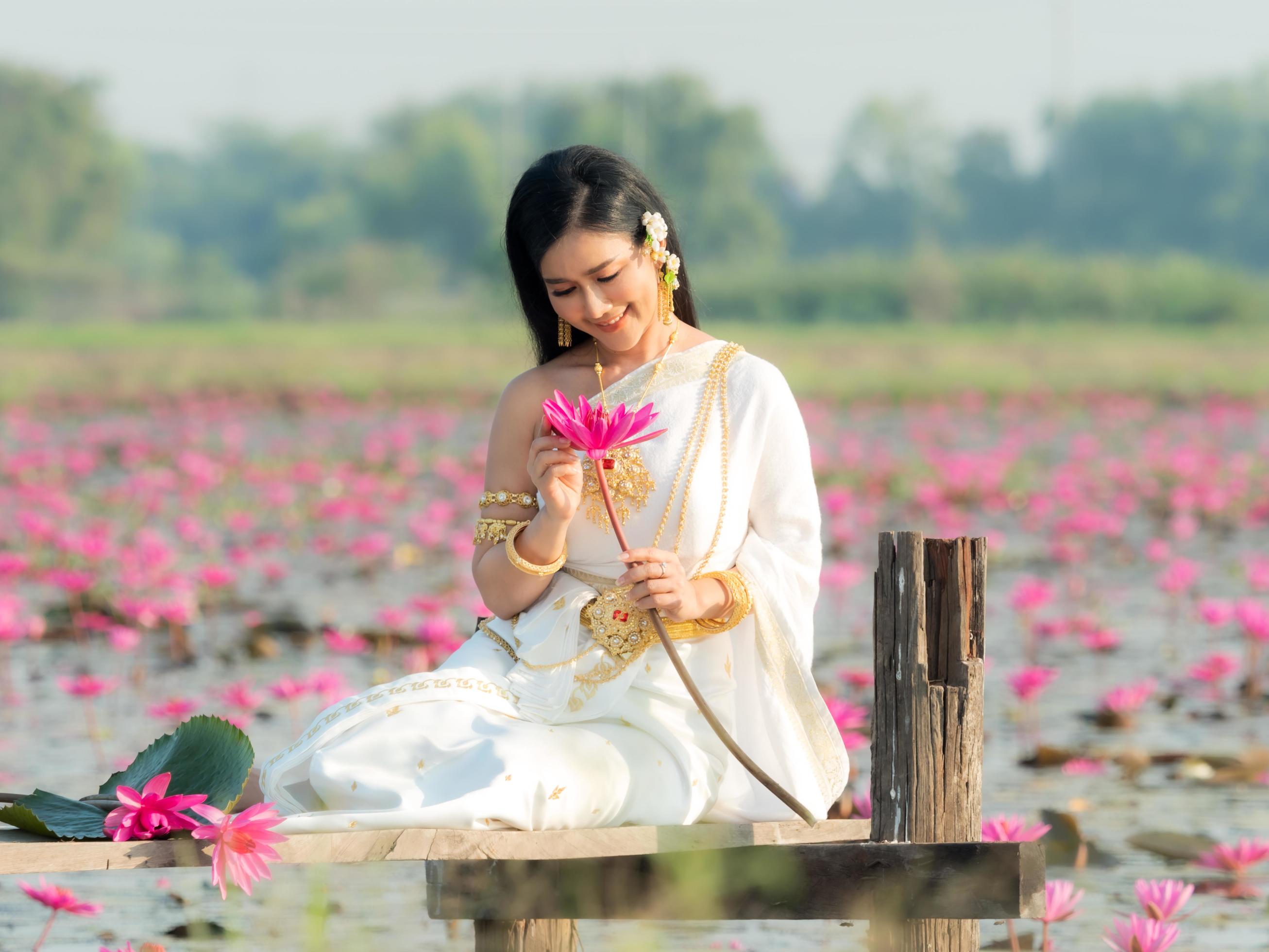 An elegant Thai woman wearing traditional Thai clothes carrying lotus flowers collected from a lotus field Stock Free