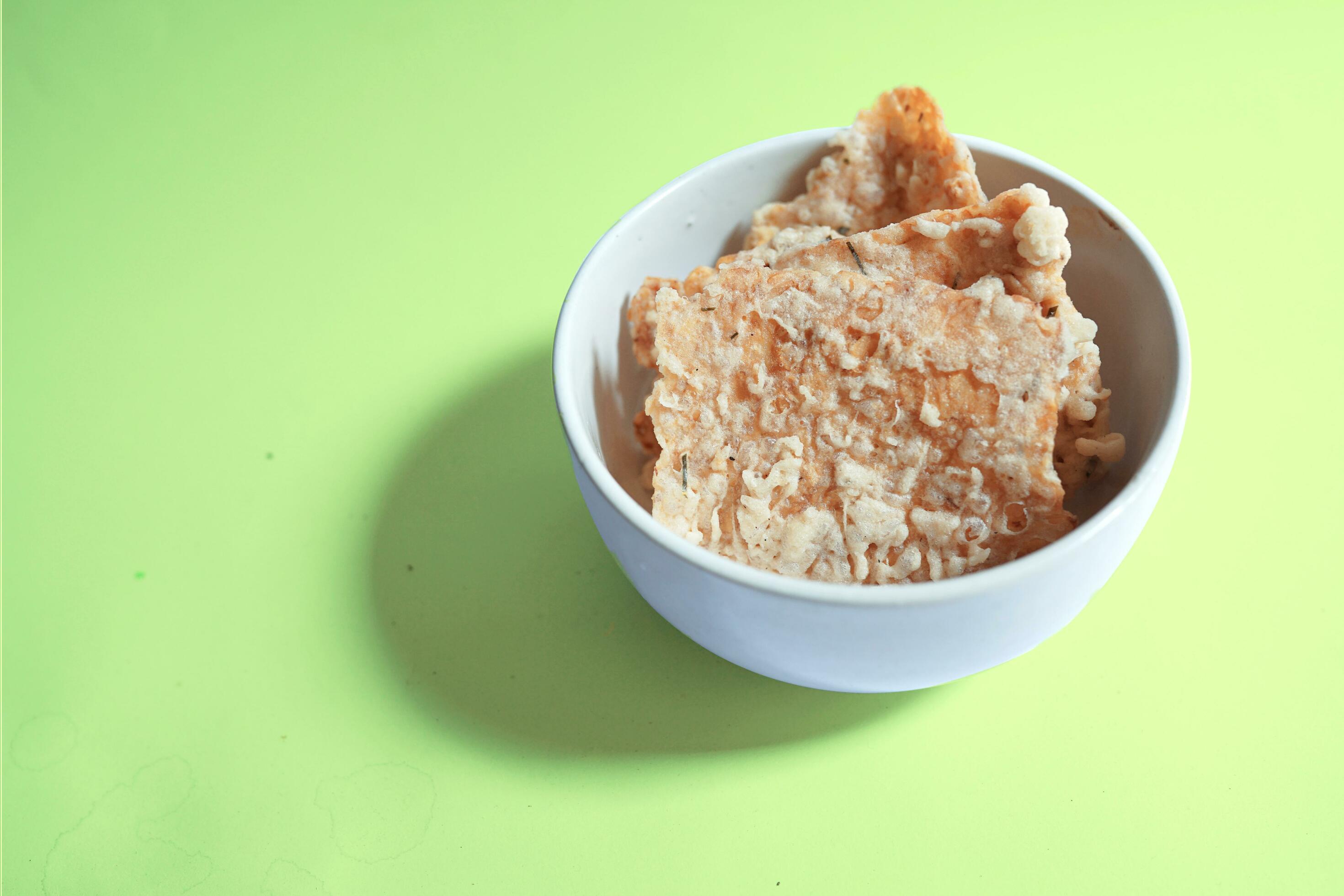 savory snack, tempeh chips in a white bowl on a green background – Indonesian street food Stock Free