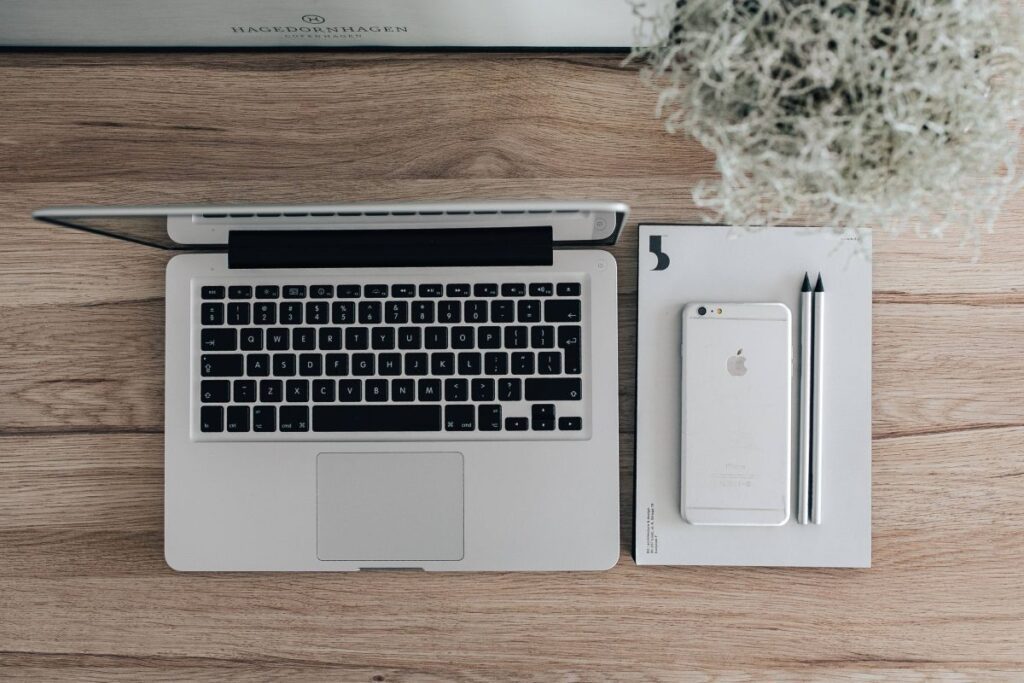 Silver Acer laptop on a wooden desk with a green plant, pencils and an Apple iPhone Stock Free