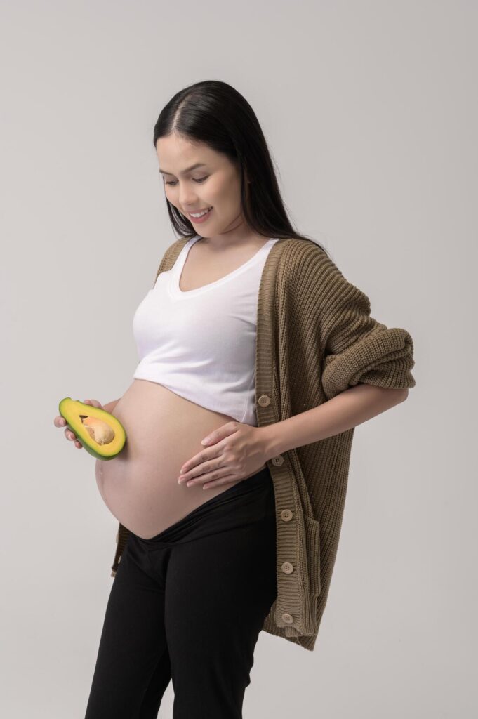 Portrait of Beautiful pregnant woman holding avocado over white background studio, health and maternity concept Stock Free