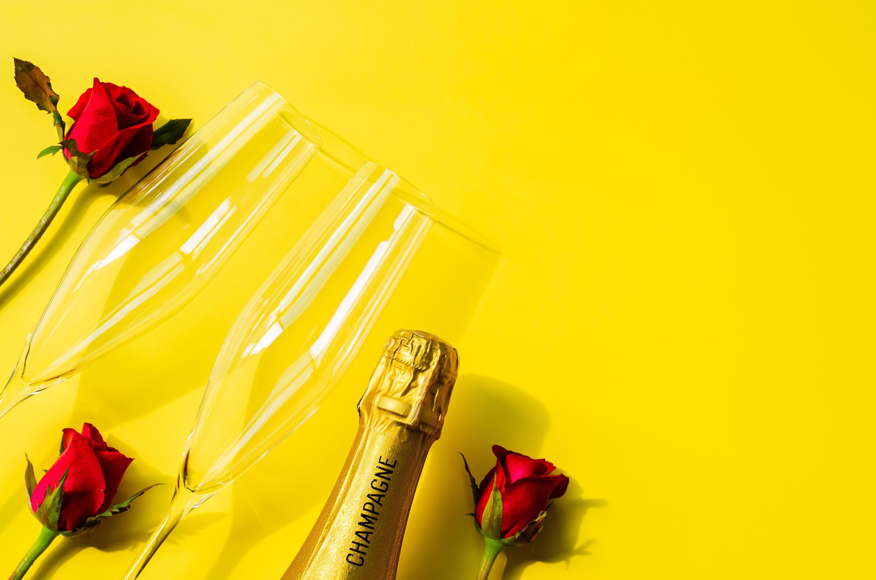 Champagne bottle with two glasses and rose flowers on yellow background Stock Free