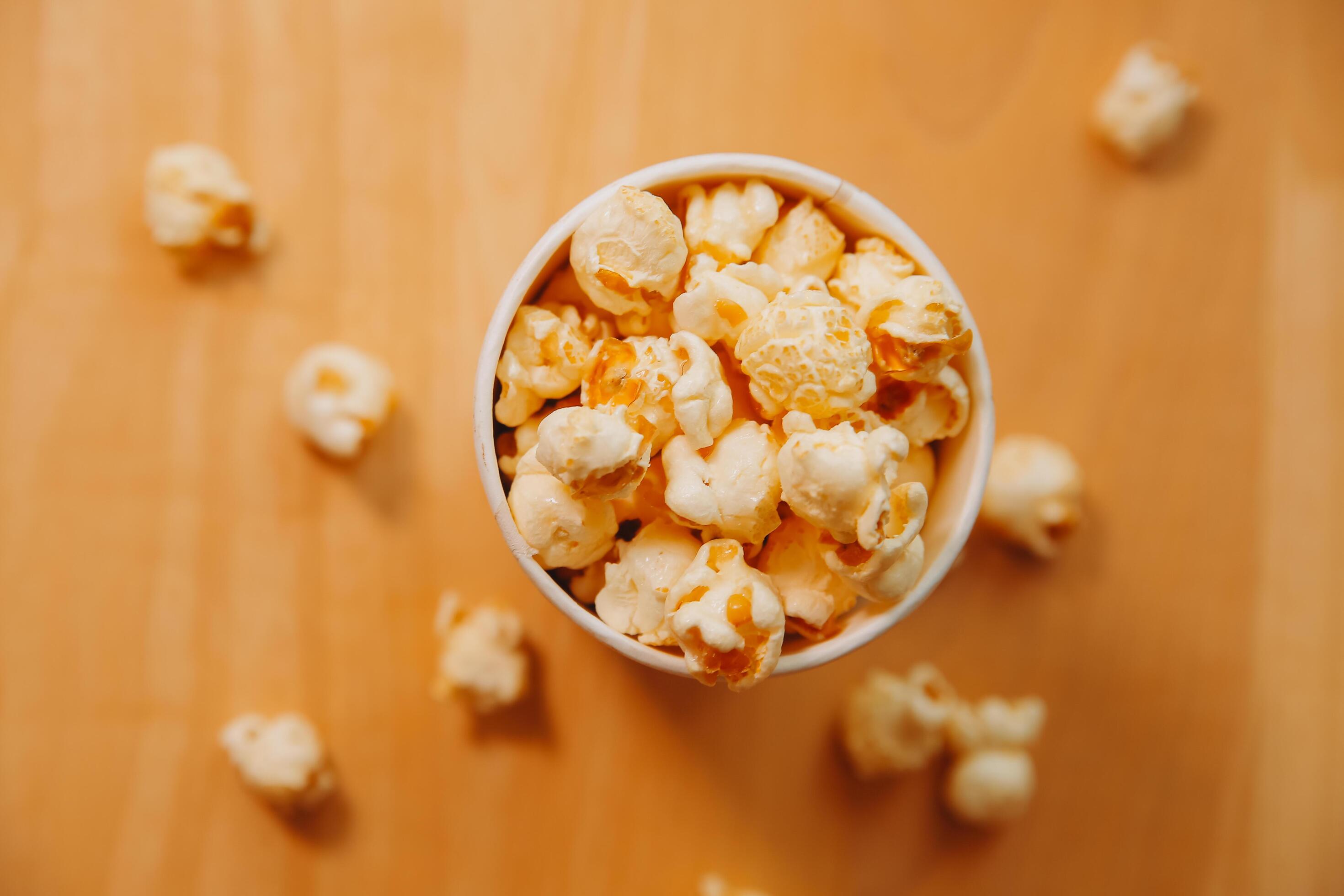 A bucket of popcorn, top-view, warm colors, light brown wooden background, flat lay, daylight macro close-up Stock Free