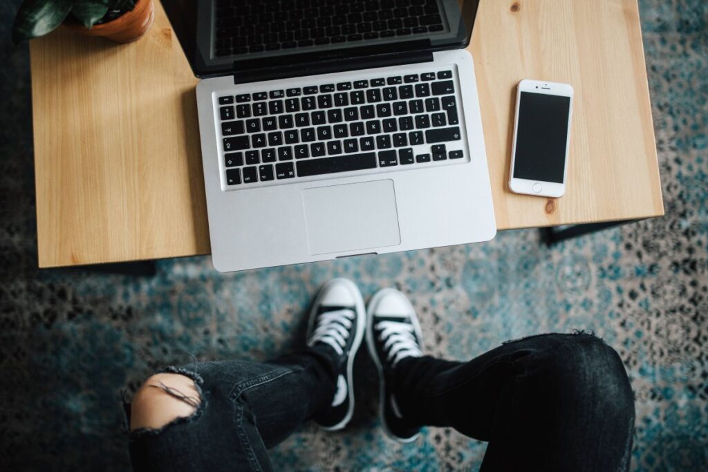 Woman in ripped jeans and black sneakers with a silver laptop on a wooden table Stock Free