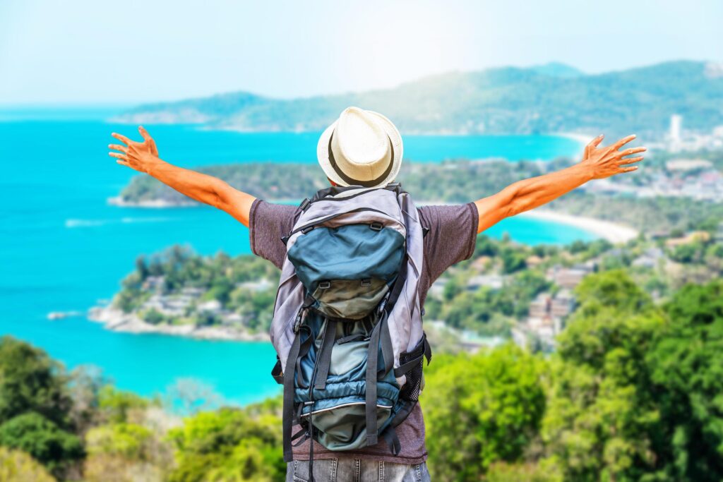 Rear view portrait of young man traveler with backpack standing on a mountain with arms spread open, Travel Life style and Adventure concept. Stock Free