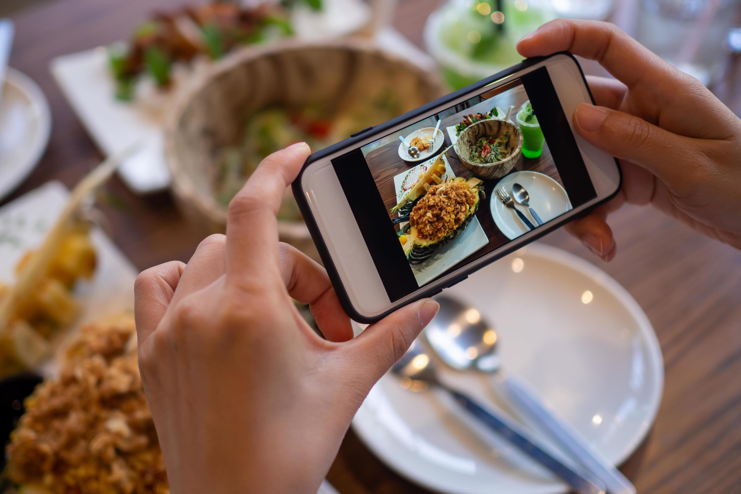 Woman using mobile phone to take pictures of food on the table. Taken on mobile and put on social networks. Stock Free