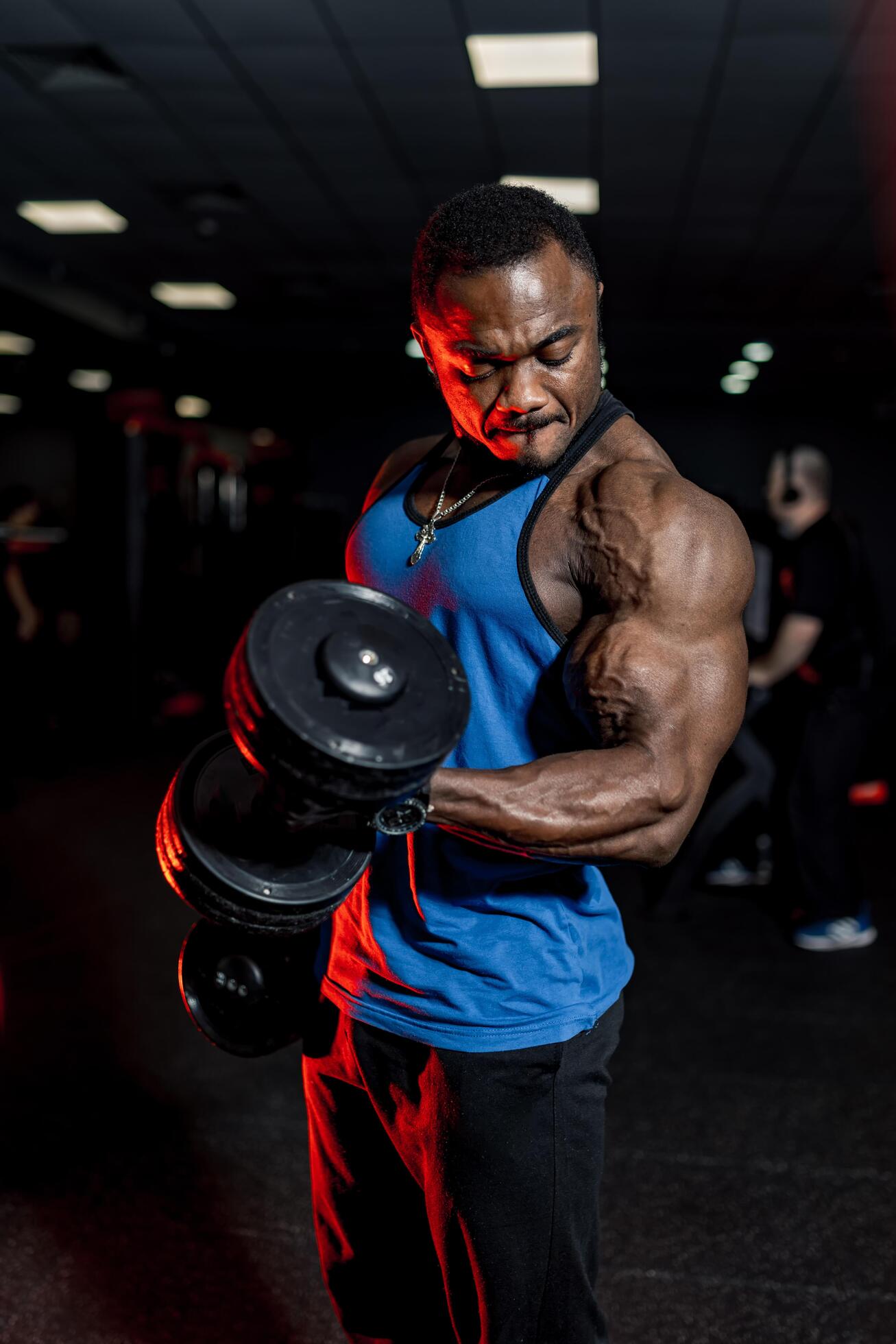 Professional african american sportsman posing on camera in sport clothes and dumbbells in hand. Black gym background. Muscular perfect body. Stock Free