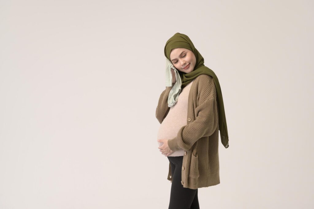 Portrait of Pregnant muslim woman in hijab holding baby cloth over white background studio Stock Free