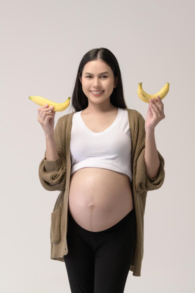 Portrait of Beautiful pregnant woman holding banana over white background studio, health and maternity concept Stock Free