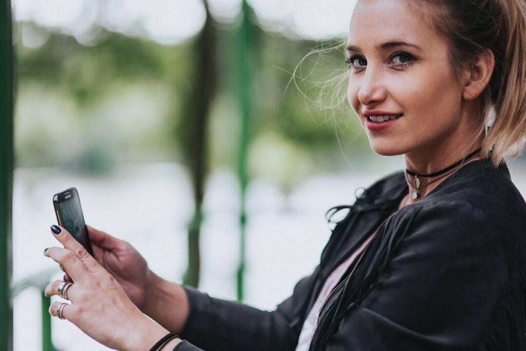 Blonde woman in a black jacket and ripped jeans by a green handrail Stock Free