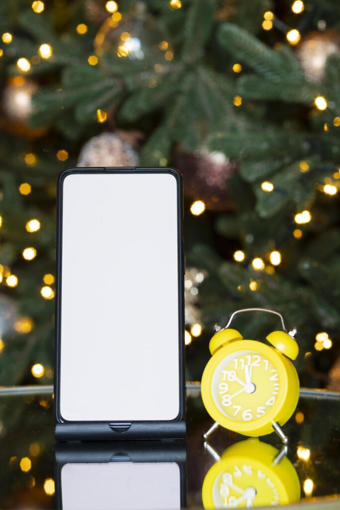 Phone with isolated screen and clock alarm on the background of the Christmas tree, bokeh and garland. New year gift, sales and offers. Stock Free