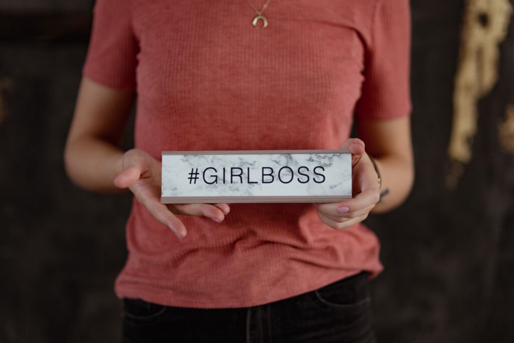 A young woman is holding a Girlboss Desk Sign Stock Free