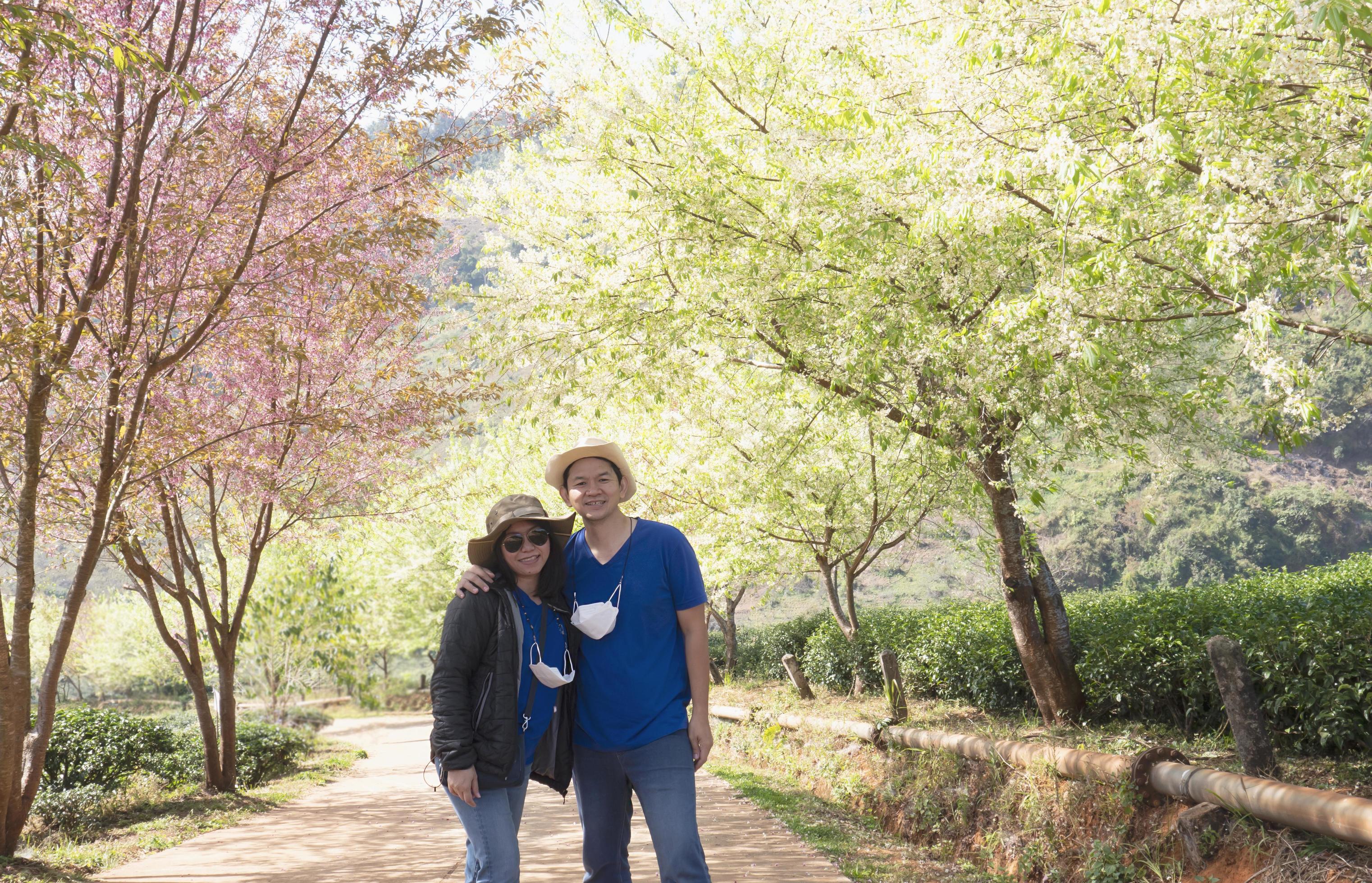 Asian couple happy taking photo in beauliful nature Prunus cerasoides Sakura of Thailand flower garden in Doi Ang Khang, Chiangmai Thailand Stock Free