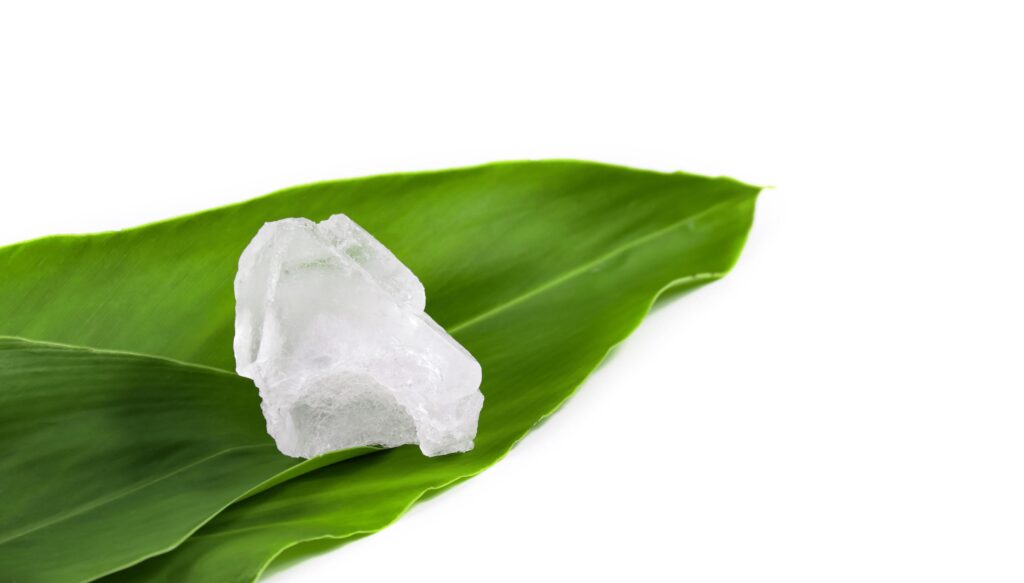 White crystal clear alum cube on green leaf isolated on white background. Stock Free