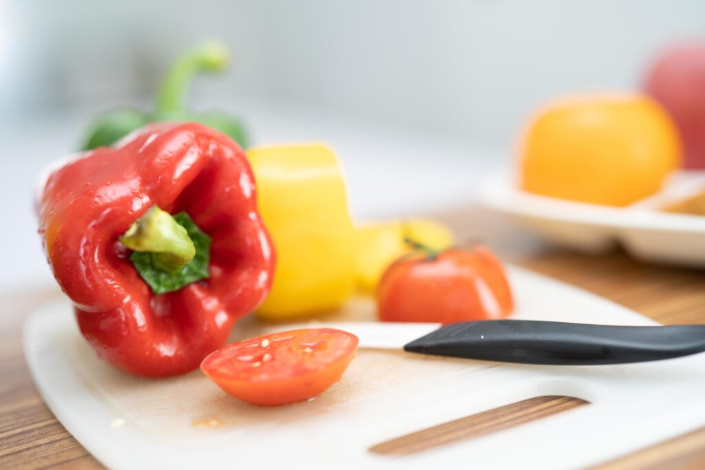 Red bell sweet pepper and tomato with knife on cutting board, vegetable salad, cooking healthy food Stock Free